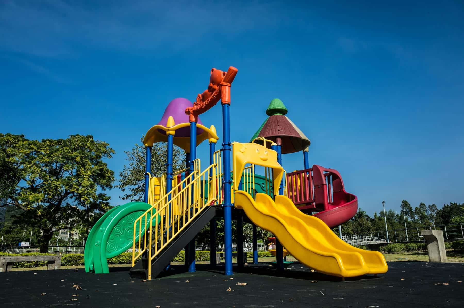 A bright play structure with a yellow slide on a rubber safety surface under a blue sky