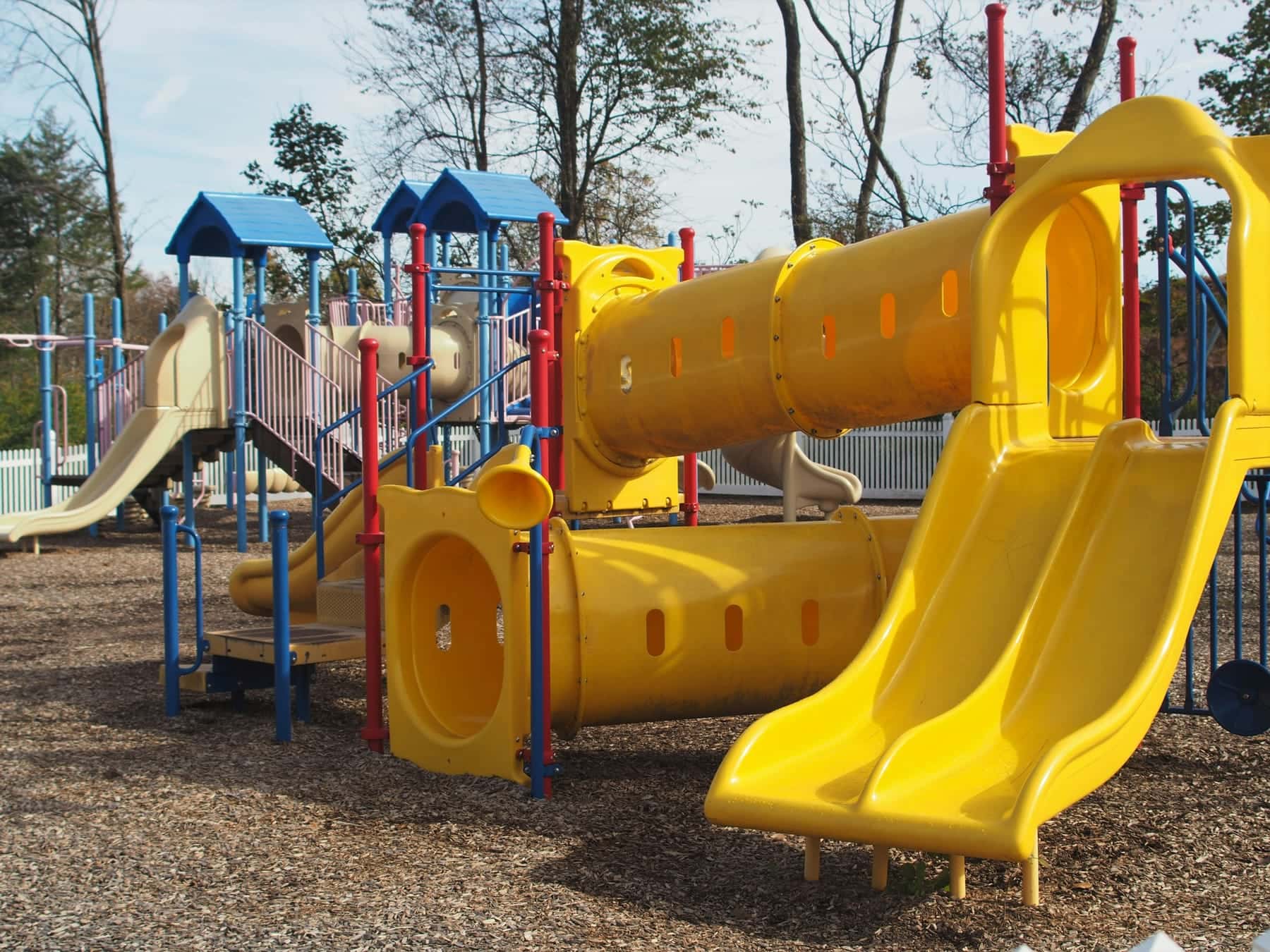 A yellow tube slide and a wide slide on a play structure over wood chips